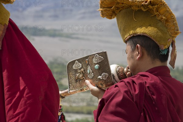 A Buddhist monk playing a dung dkar, the Tibetan conch shell drum, standing on the roof of Thikse Gompa, the large, Buddhist monastery in Ladakh. Many inhabitants of this Indian region, which is often called Little Tibet, follow the Tibetan Buddhism. Leh District, Union Territory of Ladakh, India, Asia
