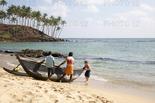 Tourist boy helping local men to launch their fishing canoe, Mirissa, Sri Lanka, Asia