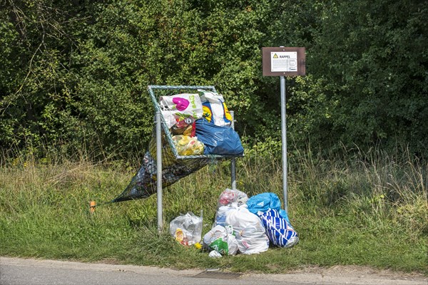 Illegal dumping of household refuse bags in net along roadside meant for throwing in cans and plastic bottles