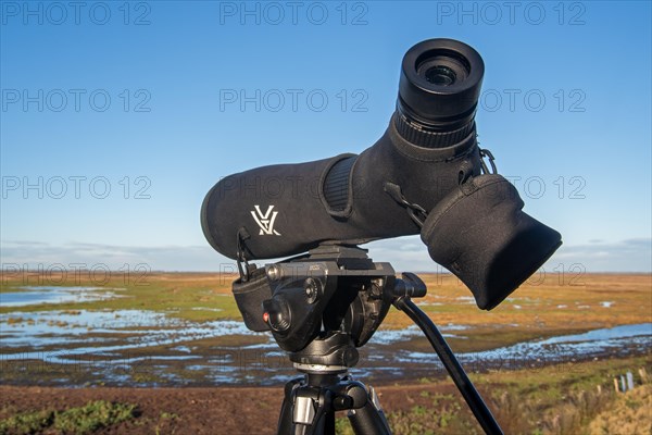 Birdwatcher's telescope and view over salt marsh of the Western Scheldt estuary at nature reserve Verdronken Land van Saeftinghe, Netherlands