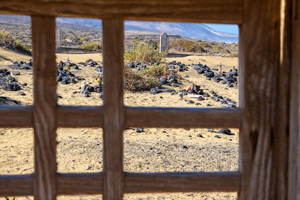 View through old gate cemetery gate cemetery door on old silted up historic cemetery from 1950s with several graves marked by stones from abandoned village village Cofete on west coast of peninsula Jandia, in the background mountains hills former volcanoes, Cofete, Jandia, Fuerteventura, Canary Islands, Canary Islands, Spain, Europe