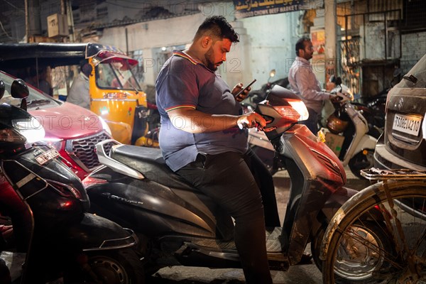 Man on scooter standing in a traffic jam looking at his mobile phone, Hyderabad, Andhra Pradesh, India, Asia