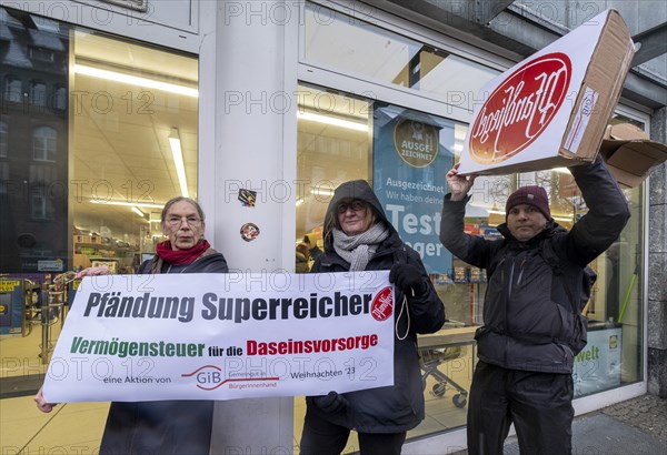 Germany, Berlin, 21.12.2023, action by Gemeingut in BuergerInnenhand (GiB), actions in front of branches of LIDL, Aldi and BMW, here a Lidl branch in Luisenstrasse / Berlin-Mitte, activists press a large deposit seal on a door of the LIDL branch, Carl Wassmuth (right), spokesman for Gemeingut: Super-rich people like LIDL owner Dieter Schwarz only pay tiny tax rates, Europe