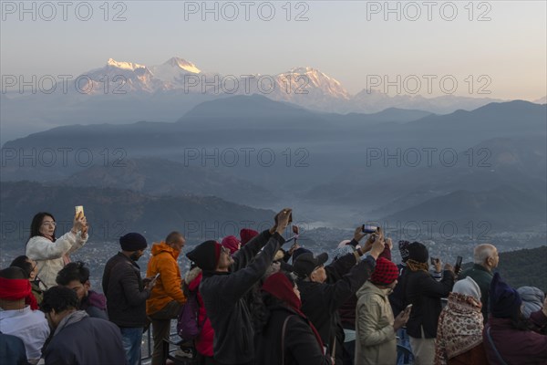 Asian-looking tourists watching and photographing sunrise as well as shooting selfies on the second day of the 2024 year from Sarangkot, with mountains of the Annapurna Massif in the background. Pokhara, Kaski District, Gandaki Province, Nepal, Asia