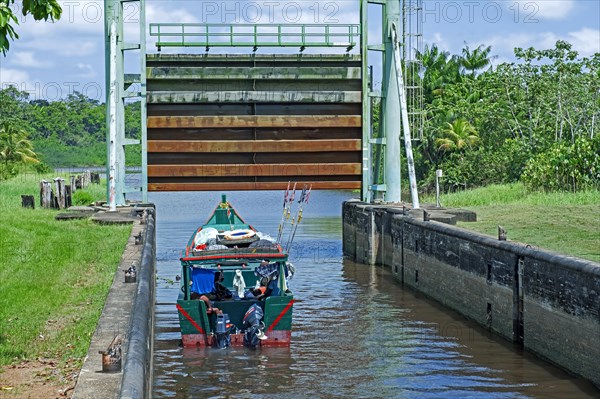 Small traditional wooden fishing boat leaving lock, sluice gate on the Saramacca River at the village Uitkijk, Saramacca District, Suriname, Surinam, South America