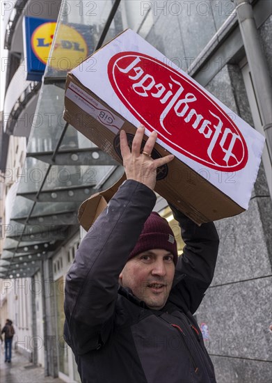 Germany, Berlin, 21.12.2023, action by Gemeingut in BuergerInnenhand (GiB), actions in front of branches of LIDL, Aldi and BMW, here a Lidl branch in Luisenstrasse / Berlin-Mitte, activists press a large deposit seal on a door of the LIDL branch, Carl Wassmuth (photo), spokesman for Gemeingut: Super-rich like LIDL owner Dieter Schwarz only pay tiny tax rates, Europe