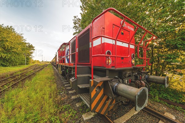 Red locomotive standing on tracks next to green trees under a cloudy sky, Lower Rhine, North Rhine-Westphalia, Germany, Europe