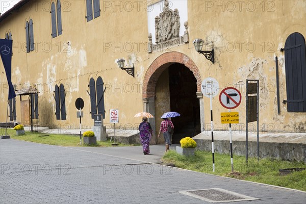 Women walking with umbrellas for shade towards the fort doorway exit in the historic town of Galle, Sri Lanka, Asia