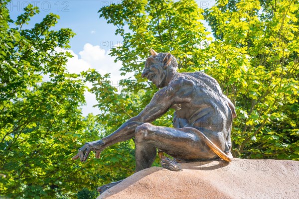 Bronze statue depicting a grinning, laughing naked fantasy figure, placed on a rock, statue, plastic, sculpture, bronze devil with horns, long ears, tail, hairy back and shoulders and goat's foot, hoof, on a boulder, part of the group of figures with homunculus and witch grandmother Wadelinde, Hexentanzplatz, Thale, Eastern Harz, Harz Mountains, Saxony-Anhalt, Germany, Europe