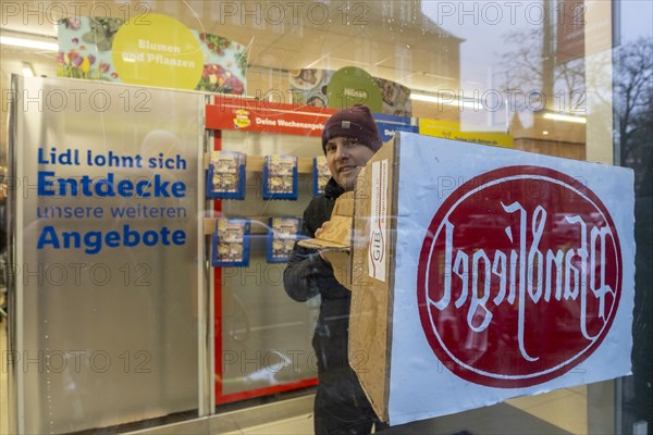 Germany, Berlin, 21.12.2023, action by Gemeingut in BuergerInnenhand (GiB), actions in front of branches of LIDL, Aldi and BMW, here a Lidl branch in Luisenstrasse / Berlin-Mitte, activists press a large deposit seal on a door of the LIDL branch, Carl Wassmuth (photo), spokesman for Gemeingut: Super-rich like LIDL owner Dieter Schwarz only pay tiny tax rates, Europe