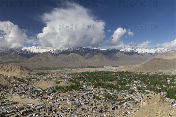 Leh, the capital town of Ladakh and main settlement in the region, with the Indus Valley below and the Stok Range of the Zanskar Mountain, Himalayas, in the distance. Seen from Namgyal Tsemo, The Victory Hill, with a big, white cloud on the otherwise fairly clear, blue sky. Photographed in late May, the springtime. District Leh, Union Territory of Ladakh, India, Asia