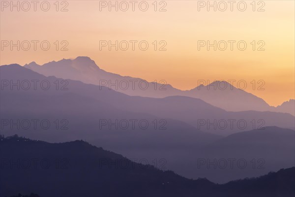 Silhouette of the Himalayan peaks, including Himalchuli and Baudha Himal, backlit by the orange sky, seen shortly before sunrise on a January, winter morning from Sarangkot, the popular viewpoint above Pokhara. Kaski District, Gandaki Province, Nepal, Asia
