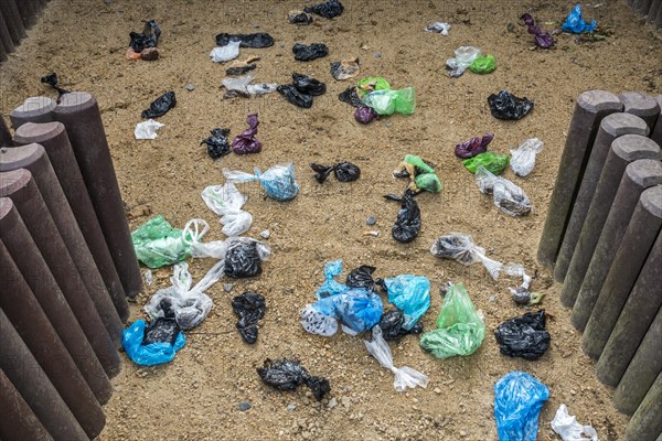 Fenced sandy public dog toilet area in city park filled with colourful discarded plastic dog poop bags