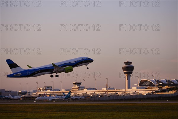 AirBaltic Airbus A220 taking off on Runway South with Terminal 1 and Tower in the sunset, Munich Airport, Upper Bavaria, Bavaria, Germany, Europe