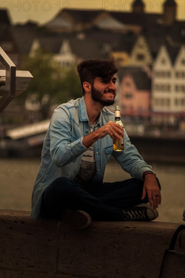 A man sits on the riverbank enjoying a drink in the evening, Hohenzollernbruecke, Cologne Deutz, North Rhine-Westphalia, Germany, Europe