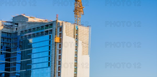 Yellow crane elevator attached to side of building that is under construction against a clear blue sky