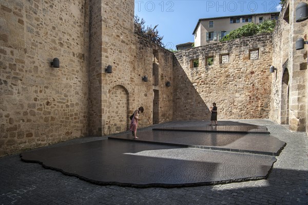 Tourists visiting giant replica of the Rosetta Stone that allowed Jean-Francois Champollion to decipher the Egyptian hieroglyphs, Place des Ecritures, Figeac, Lot, Midi-Pyrenees, France, Europe