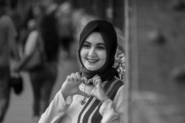 Friendly smiling woman in hijab making a heart sign with her hands, Hohenzollernbruecke, Cologne Deutz, North Rhine-Westphalia, Germany, Europe