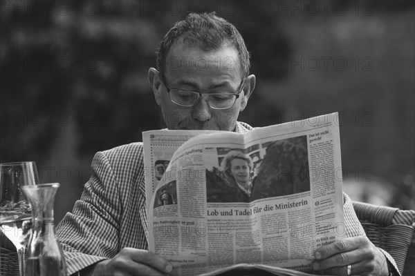 A man engrossed in reading a newspaper at an outdoor table, Wuppertal Elberfeld, North Rhine-Westphalia, Germany, Europe