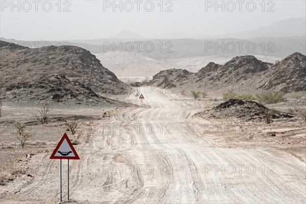 A warning sign stands in front of a sandy desert road, Safari, GravelRoad, unpaved roads, gravel roads, gravel surface, Namibia, Africa