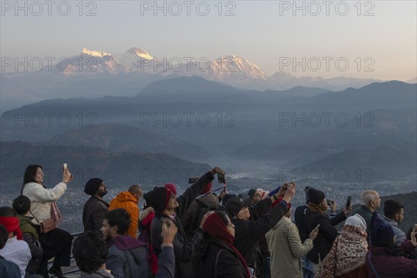Asian-looking tourists watching and photographing sunrise as well as shooting selfies on the second day of the 2024 year from Sarangkot, with mountains of the Annapurna Massif in the background. Pokhara, Kaski District, Gandaki Province, Nepal, Asia