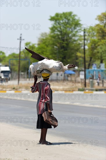 African woman carrying scrap metal on her head through the streets, street scene, Kongola in Namibia