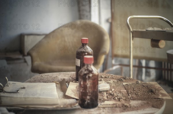 An old cloudy bottle on a dirty table next to a rusty hospital trolley, urologist's villa Dr Anna L., Lost Place, Bad Wildungen, Hesse, Germany, Europe