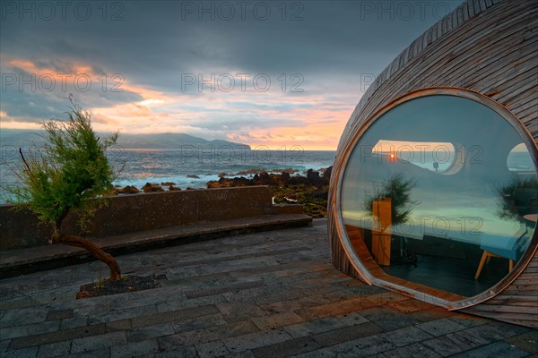 Round window of the wooden extension of the famous Calla Bar and view of the coast at sunset, Madalena, Pico, Azores, Portugal, Europe