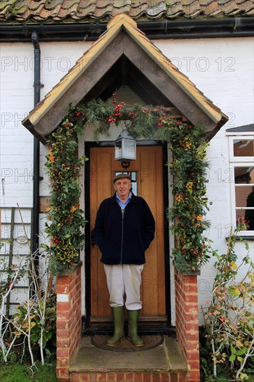Elderly man standing in his porch having decorated it for Christmas, Suffolk, England, UK