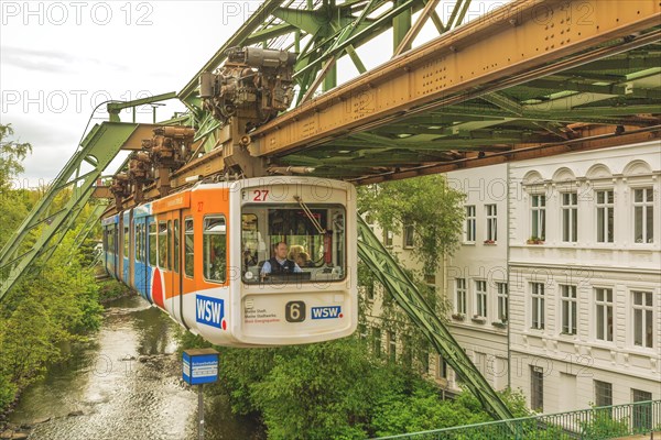 Suspension railway crossing a bridge in the city, river and buildings in the background, suspension railway, Wuppertal, North Rhine-Westphalia, Germany, Europe