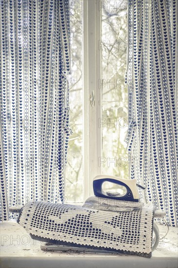 An old iron on a lace fabric in front of a window with blue curtains, urologist's villa Dr Anna L., Lost Place, Bad Wildungen, Hesse, Germany, Europe