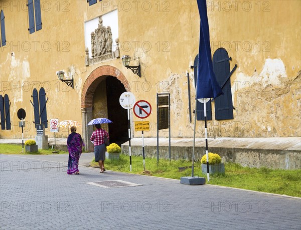 Women walking with umbrellas for shade towards the fort doorway exit in the historic town of Galle, Sri Lanka, Asia
