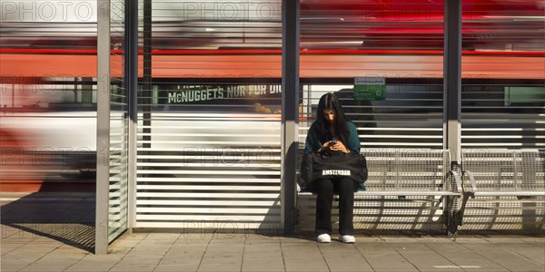 Young woman sitting on the platform looking at her mobile phone while a train passes by, Giessen Central Station, Hesse, Germany, Europe