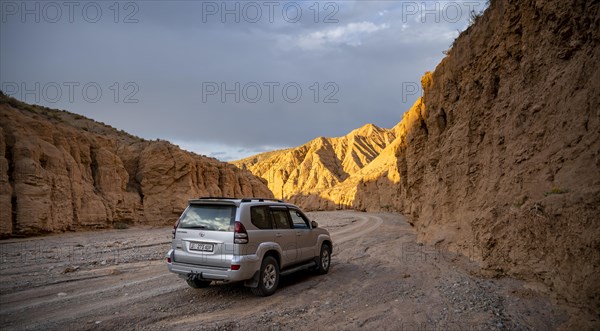 Car driving on a winding road in a gorge while the evening sun illuminates the mountains, Kyrgyzstan, Asia