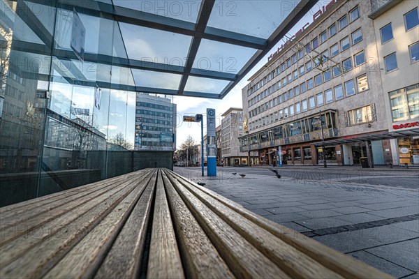 View along a wooden bench onto a square with glass walls and buildings, Leopoldplatz, Pforzheim, Germany, Europe