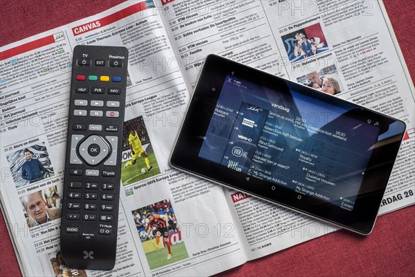 Remote control and tablet showing television channels on top of open Belgian magazine showing the tv programmes' pages