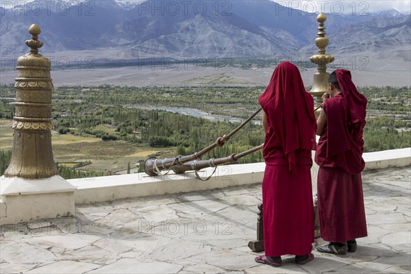 Monks playing Tibetan horns, dungchens, standing on the roof of Thikse Gompa, a large, Buddhist monastery in Ladakh overlooking the Indus Valley. Many inhabitants of this Indian region, which is often called Little Tibet, follow the Tibetan Buddhism. Leh District, Union Territory of Ladakh, India, Asia