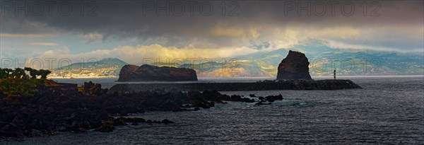 Dark clouds over a calm sea with the island of Faial in the distance and the rock formations Ilheu em Pe and Ilheu Deitado during an atmospheric sunset, Madalena, Pico, Azores, Portugal, Europe