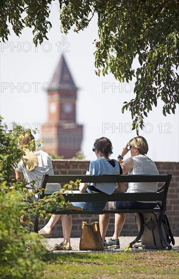 Swedish woman sitting on a park bench, behind them the tower of the town hall, Helsingborg, Skane laen, Sweden, Europe