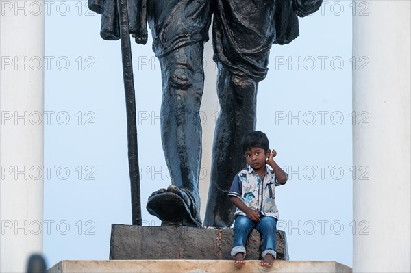 Child at the foot of a Mahatma Gandhi monument, statue, former French colony of Pondicherry or Puducherry, Tamil Nadu, India, Asia