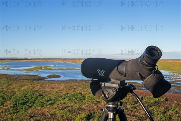 Birdwatcher's telescope and view over salt marsh of the Western Scheldt estuary at nature reserve Verdronken Land van Saeftinghe, Netherlands
