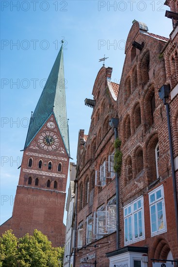 Historic town houses and merchants' houses, gables of traditional brick buildings, and tower of St John's Church on the town square Am Sande, North German gabled houses, old town, blue sky on a sunny day, Lueneburg, Lower Saxony, Germany, Europe