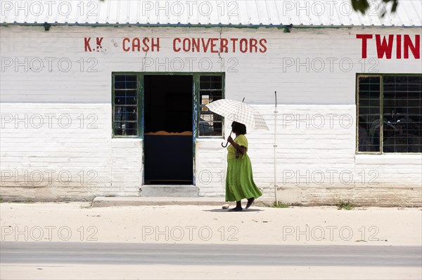 African woman, African woman in front of a shop, street, human, street scene, population, walking, city, urban, umbrella, sun protection, climate, climate change, Kongola in Namibia