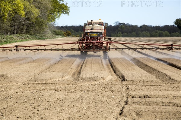 Farm machinery spraying an arable field of bare soil, Shottisham Suffolk, England, UK