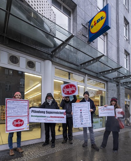 Germany, Berlin, 21.12.2023, action by Gemeingut in BuergerInnenhand (GiB), actions in front of branches of LIDL, Aldi and BMW, here a Lidl branch in Luisenstrasse / Berlin-Mitte, activists press a large deposit seal on a door of the LIDL branch, Carl Wassmuth, spokesman for Gemeingut: Super-rich like LIDL owner Dieter Schwarz only pay tiny tax rates, Europe
