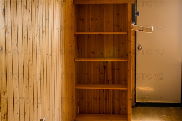 Empty built-in bookcase near door of abandoned rustic cabin with sun shining through unseen window