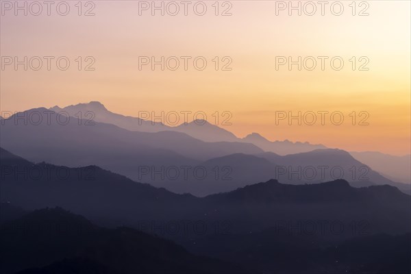 Silhouette of the Himalayan peaks, including Himalchuli and Baudha Himal, backlit by the orange sky, seen shortly before sunrise on a January, winter morning from Sarangkot, the popular viewpoint above Pokhara. Kaski District, Gandaki Province, Nepal, Asia