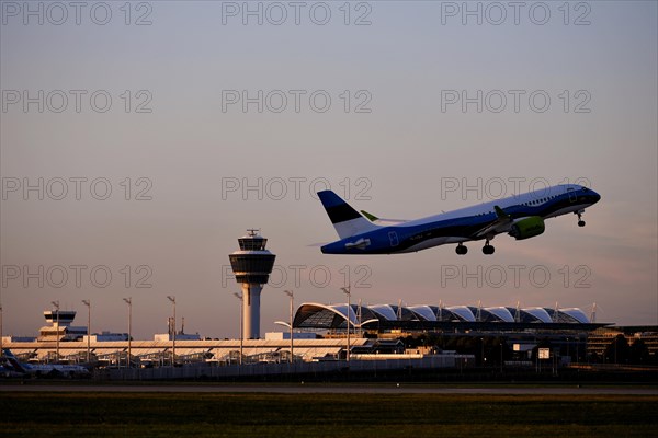 AirBaltic Airbus A220 taking off on Runway South with Terminal 1 and Tower in the sunset, Munich Airport, Upper Bavaria, Bavaria, Germany, Europe