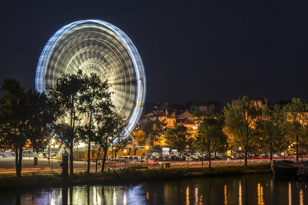 Motion blurred Ferris wheel at night along the Rhone river in the city Avignon, Vaucluse, Provence-Alpes-Cote d'Azur, France, Europe