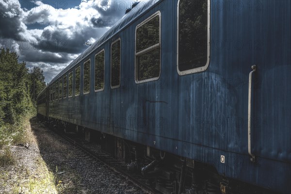 Blue carriage of a train on abandoned tracks surrounded by nature and dramatic clouds, Dornap-Hahnenfurth station, Wuppertal, North Rhine-Westphalia, Germany, Europe